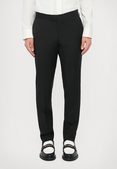 Čierne upravené nohavice s rovnými nohavicami, vyrobené z hladkej látky. Majú úzky pás a postranné úpravy. Nosené s čiernymi topánkami.