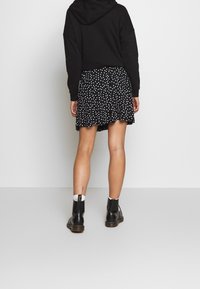 Schwarzer, verkürzter Hoodie kombiniert mit einem schwarzen Rock mit weißen Polka-Dots. Modell trägt schwarze Stiefeletten. Glatte Textur, lässiges Design.
