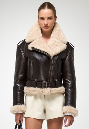 Bruine leren jas met een fluffy beige sheepskin kraag en manchetten, met een ritssluiting aan de voorkant, twee zakken en een ontwerp met een ceintuur in de taille.