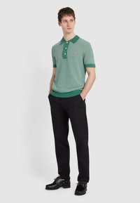 Zielona i biała w paski koszulka polo z krótkim rękawem, z jednolitą zieloną kołnierzykiem i mankietami, w połączeniu z czarnymi spodniami i czarnymi butami.