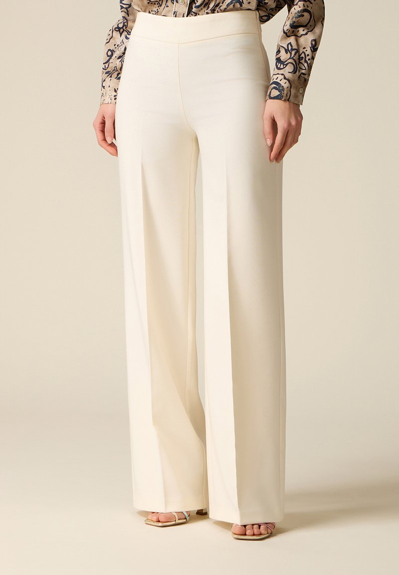 Pantaloni crem cu talie înaltă și pantaloni evazați, asortați cu o bluză cu mâneci lungi, cu model, și sandale cu vârf deschis și toc gros.