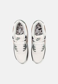 Nike-sneakers med ovandel av vitt canvas, gröna accenter, grå paneler, vita snören och ett mönstrat innersulor. Platt gummisula.