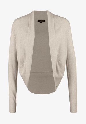 Woman wearing beige cardigan, black top, distressed blue skinny jeans, black ankle boots, and a black crossbody bag, standing with hand on hip.