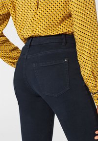 Jeans azul marino de cintura alta, ajustados y con bolsillos traseros. Combinados con una blusa amarilla de estampado geométrico con pequeños triángulos.