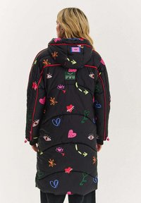 �Černý prošívaný kabát s barevnými vyšívanými vzory, obsahujícími srdce, oči a květiny. Kabát má kapuci a elastické manžety.