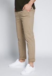 Chino beige con una vestibilità slim, dotati di cinque tasche e orli arrotolati, abbinati a sneakers bianche. Tessuto in cotone liscio.