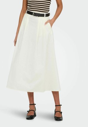 Femme portant une jupe midi blanche plissée, une ceinture noire, un haut sans manches rayé et des talons noirs à bride à la cheville, debout avec une main dans la poche.