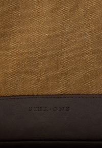 Καφέ καμβάς με υφή και σκούρο δερμάτινο κάτω μέρος με ανάγλυφο λογότυπο "PIER ONE". Απλός και δομημένος σχεδιασμός.