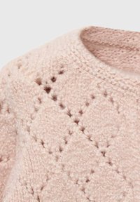 Měkký růžový pletený svetr s texturovaným diamantovým vzorem a kolem krku, ukazující detailní pletené stehy.