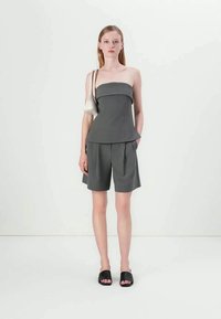 Top gri mulat fără bretele, cu talie peplum, asortat cu pantaloni scurți. Modelul poartă sandale negre plate și ține o geantă albă mică.