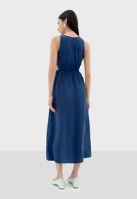 Vestido maxi sin mangas de color azul marino con cintura ajustada, textura suave y dobladillo hasta la rodilla, combinado con zapatos plateados de tipo slip-on.
