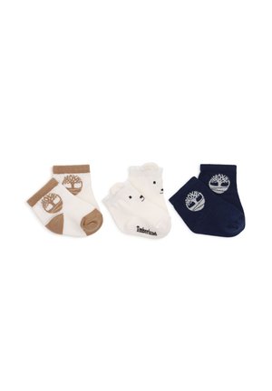 Trois paires de chaussettes pour bébé en blanc et marron, blanc avec des visages d’ours, et bleu marine avec des logos d’arbres, disposées côte à côte sur fond blanc.