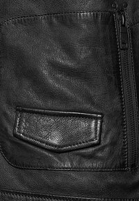 Musta nahkatakki, jossa on teksturoitu pinta, vaakasuora vetoketjutasku ja monimutkainen ompelu reunoilla.