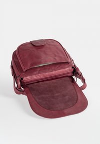 Bordeauxroter Leder-Rucksack mit glatter Textur, Klappverschluss, vorderer Reißverschlusstasche und einem großen, weichen, wildlederähnlichen Riemen.