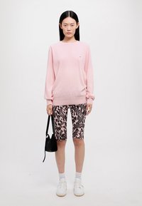 Maglione rosa chiaro, pantaloni shorts a stampa leopardata con dettagli neri, calze bianche e sneaker; porta una piccola borsa a tracolla nera.