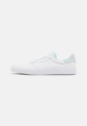 Hvid lavtopet sneakers med diskret lysegrøn hælkappe og polstret krave, med hvide snørebånd og tekstureret sål.