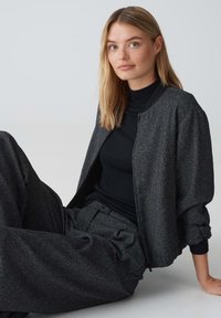 Schwarze, strukturierte Bomberjacke, kombiniert mit einem schwarzen Rollkragenpullover und passenden weit geschnittenen Hosen; entspannte Passform mit subtiler Oberfläche und gerippten Akzenten.