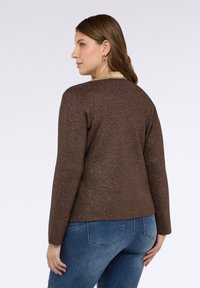 Brun metallic långärmad topp med rund halsringning, texturerat tyg och beige detaljer vid kragen, kombinerad med blå denimjeans.