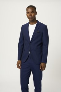 Traje azul marino hecho de una tela suave, con una chaqueta de botón simple, solapas muesca y un bolsillo en el pecho con un acento negro. Los pantalones son a juego.