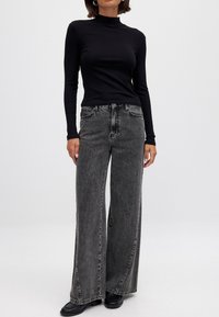 Svart ribbad turtleneck topp parat med högmidjade, vida grå jeans och svarta ankelboots. Slät tyg med subtil struktur.