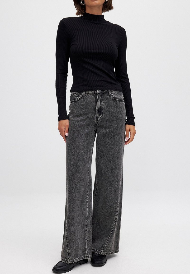 Svart ribbad turtleneck topp parat med högmidjade, vida grå jeans och svarta ankelboots. Slät tyg med subtil struktur.