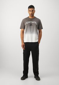 Grå til hvid gradient t-shirt med "FORTNITE" logo, parret med sorte cargo bukser med sidelommer og diskret branding. Sorte sko.