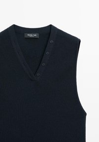 Navyblauwe mouwloze gebreide trui met een V-hals, voorzien van knoopdetails op de schouder en een geribbelde structuur. Merkenlabel zichtbaar.