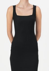 Czarna, prążkowana sukienka na ramiączkach z kwadratowym dekoltem i dopasowanym krojem. Materiał jest elastyczny i gładki w dotyku. Prosty fason, bez wzorów.