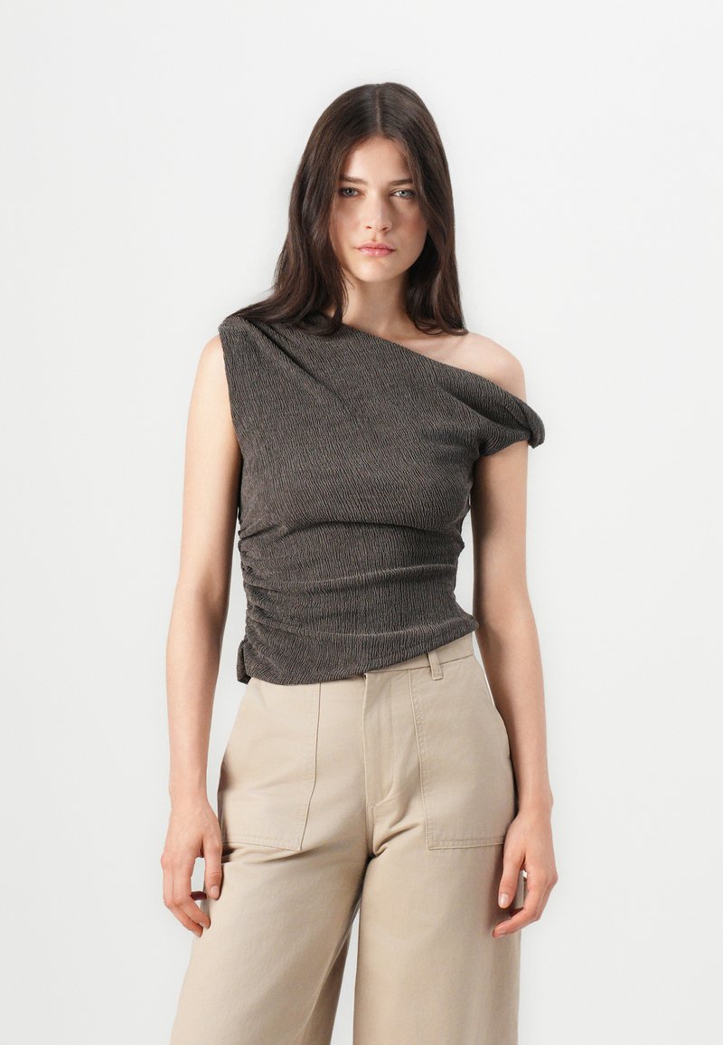 Brown one-shoulder top with gathered texture, fitted bodice, and soft fabric. Paired with beige wide-leg trousers.