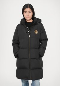 Melna pūķa jaka ar kapuci, priekšā rāvējslēdzēju un divām sānu kabatām. Aprīkota ar zelta emblēmu un quiltētu dizainu siltumizolācijai. Izstrādāta, lai nodrošinātu siltumu.