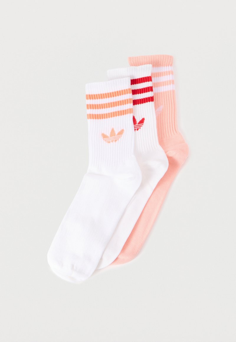 Tres pares de calcetines tobilleros: dos blancos con rayas y logotipos en naranja y rojo, y uno liso color durazno con rayas y logotipo tenues.