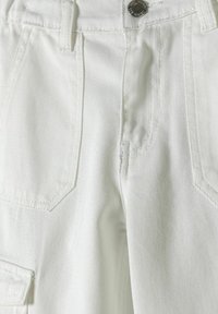 Pantalones cargo blancos de algodón texturizado, con múltiples bolsillos, cierre de botón y detalles de costura visibles.