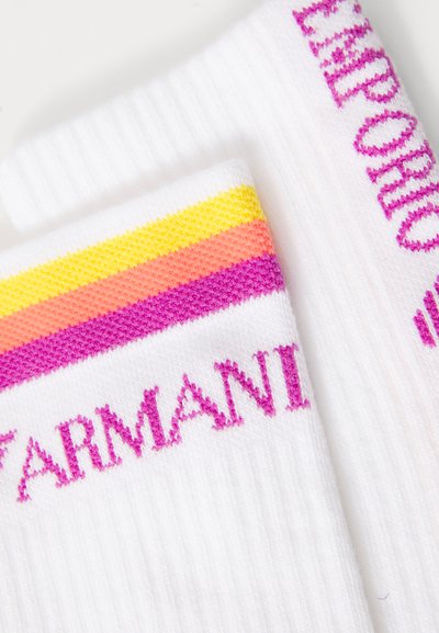 Bílé ponožky s žebrovanou texturou, s horizontálními pruhy v růžové, oranžové a žluté barvě a textem "ARMANI" v růžové barvě nahoře.