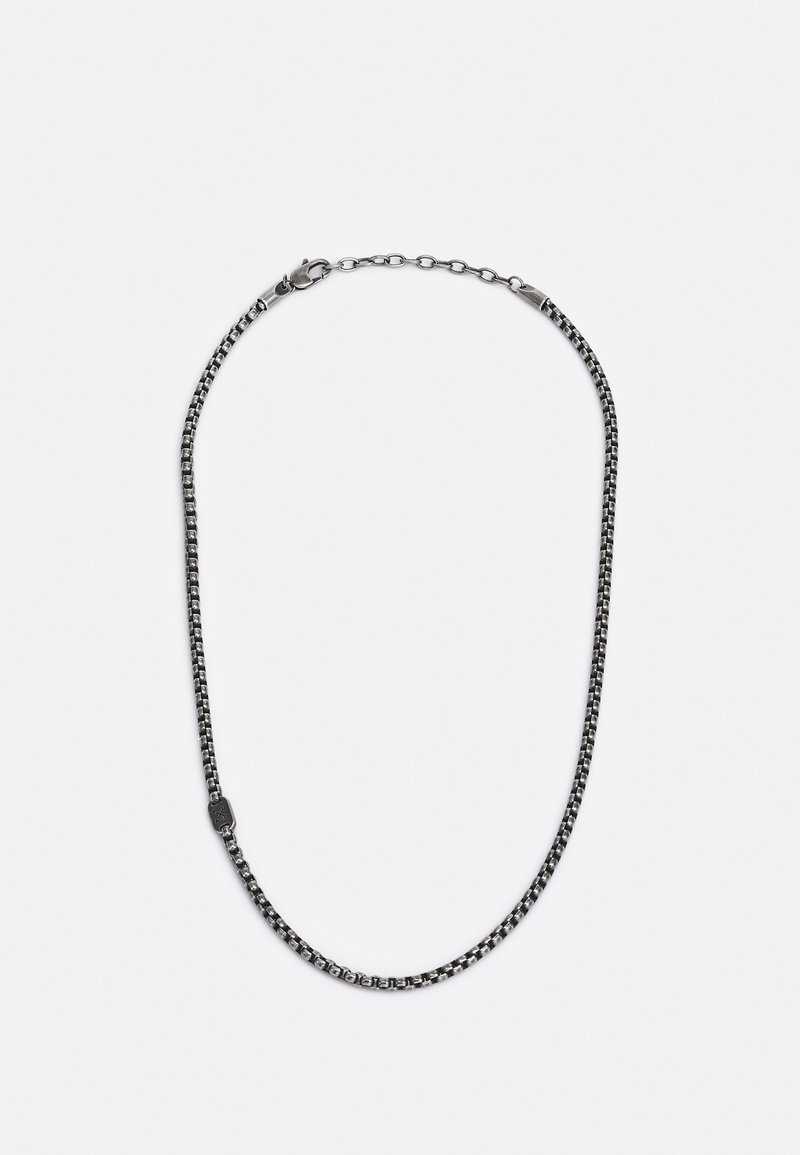 Collier chaîne à maillons carrés ton argent avec fermoir mousqueton réglable et courte chaînette d’extension sur fond blanc.