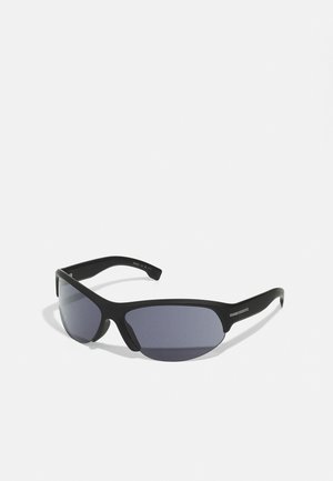 Occhiali da sole neri con un design sportivo, dotati di lenti scure, montatura opaca liscia e sottili accenti metallici sulle astine.
