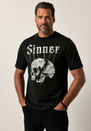 Sort bomulds T-shirt med et grafisk design af to kranier med snoreaccents og ordet "Sinner" i hvid gotisk skrifttype.