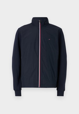 Veste bleu marine avec col montant, fermeture éclair à l'avant et manches longues. Présente des accents de fermeture éclair rouges et blancs ainsi qu'un petit logo sur la poitrine.