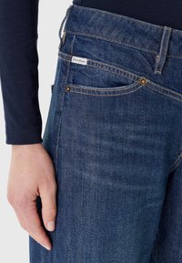 Jeans in denim blu scuro con vestibilità slim, rivetti in rame, etichetta posteriore e una sottile trama a spina di pesce sul tessuto.