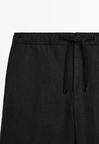 Black linen pants with a drawstring waistband, featuring a button closure and textured fabric for a lightweight appearance.