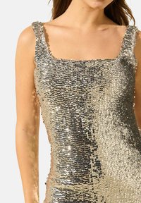 Débardeur en sequins argentés avec un décolleté carré arrondi et des bretelles larges, présentant une surface texturée et des sequins réfléchissants sur toute sa surface.