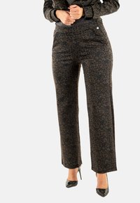 Pantalones de estampado de leopardo en marrón oscuro con una textura suave; presentan un corte ajustado y bolsillos laterales, combinados con tacones altos negros.