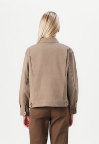 Light brown denim jacket with a pointed collar, button cuffs, and side pockets. The back features a minimalist design without embellishments.