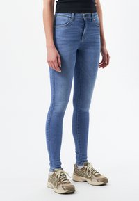 Slim-fit blå denimjeans med en blek tvätt, med midja i normalhöjd, fem fickor och stickningsdetaljer. Matchas med beige sportskor.