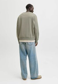 Zaļš džemperis ar apaļu izgriezumu un ribotām aprocēm, kombinēts ar gaiši ziliem džinsiem ar platu kāju griezumu. Apģērbs ir brīvā piegriezumā un ar gludu tekstūru.