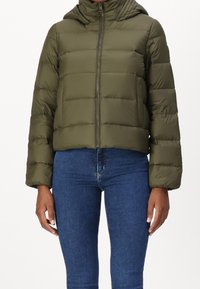 Groene pufferjas met een getailleerd ontwerp, ritssluiting en een capuchon. Heeft een doorgestikte textuur en elastische manchetten. Draagt over een blauwe spijkerbroek.