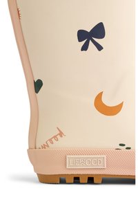 Guminis batai kreminės spalvos su rožiniais akcentais, puoštas spalvingais spaudiniais, tokiais kaip kaspinas, širdis ir pusmėnulis, tekstūruota pado dalis ir logotipo detalė.