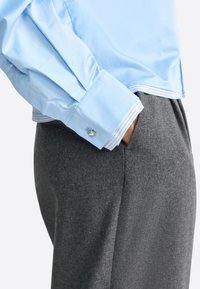Hellblaues Langarmhemd mit glänzender Textur und gestreiften Manschetten, kombiniert mit grauen strukturierten Hosen. Die Manschette verfügt über ein silbernes Knopfdetail.