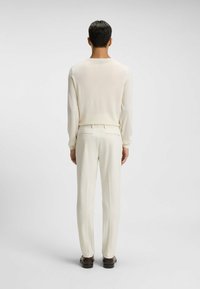 Lichtbeige gebreide top met lange mouwen, gecombineerd met crèmekleurige op maat gemaakte broeken. De outfit heeft een slanke pasvorm en een gladde textuur. Bruine schoenen maken de look af.