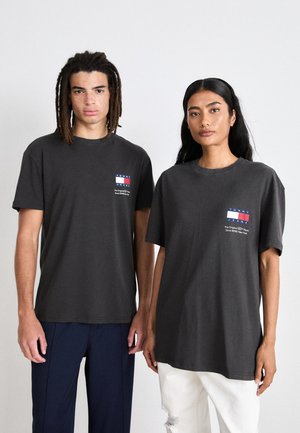 Sivé tričká s krátkymi rukávmi, s malým logom v červenej, bielej a modrej farbe na ľavej hrudi. Tkanina vyzerá mäkká, vo voľnom strihu.