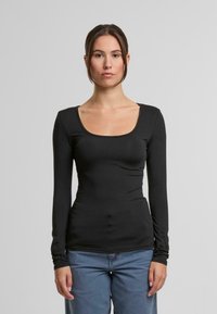 Černý dlouhý rukáv top s kulatým výstřihem, hladkou texturou a přiléhavým střihem. V kombinaci se světle modrými džínami působí vzhled neformálně a moderně.